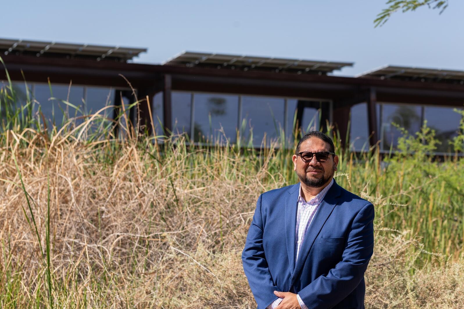 Genaro Ruiz stands in front of the Rio Salado Audubon Center and a cattail-laden pond.